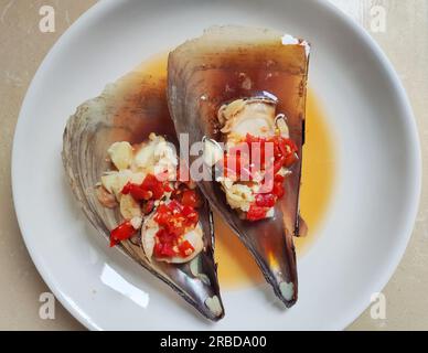 due capesante fresche al vapore con peperoni rossi speziati sul piatto da mangiare Foto Stock