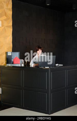 Una giovane donna lavora a un notebook in un interno buio Foto Stock