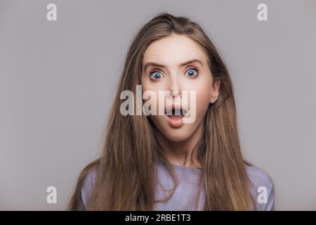 Stupita giovane donna con occhi blu, capelli scuri, fissa la fotocamera, isolata. Foto Stock