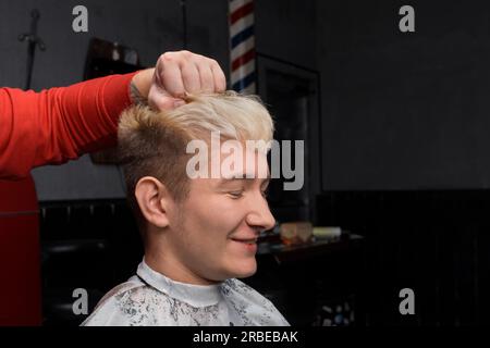 Ragazzo sorridente bel giovane aspetto europeo con occhi chiusi ritratto capelli bianchi cliente parrucchiere. Foto Stock