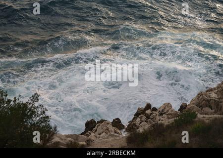 Le onde del mare che si infrangono contro le rocce della costa mediterranea durante il tramonto, contenuti del viaggio Foto Stock