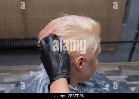 La mano di un parrucchiere di un'esperta lavoratrice in un guanto nero controlla l'acconciatura di una cliente femminile adulta. Foto Stock