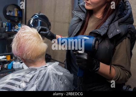 Indossa il guanto di un'esperta lavoratrice del salone, asciugando i capelli a una donna cliente servizi di parrucchiere. Foto Stock