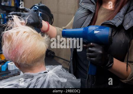 Le mani di un'esperta impiegata di una ragazza in un barbiere, asciugano i capelli con un asciugacapelli per vedere da vicino il cliente di una donna in un salone. Foto Stock