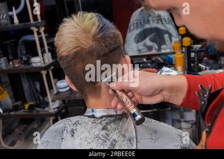 Un uomo è un barbiere europeo adulto esperto rasa la parte posteriore della testa del cliente di un ragazzo durante i servizi di parrucchiere nel salone. Foto Stock