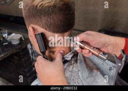 Le mani di un lavoratore professionale tagliano la testa di un giovane cliente che si occupa di parrucchiere. Foto Stock