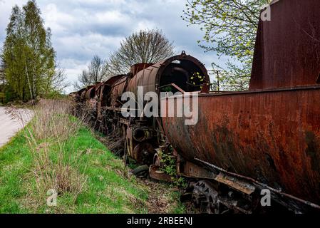 Locomotiva a steem arrugginita con carrozza a carbone abbandonata al cimitero dei treni sul vecchio binario ferroviario. Foto Stock