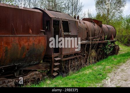 Locomotiva a steem arrugginita con carrozza a carbone abbandonata al cimitero dei treni sul vecchio binario ferroviario. Foto Stock