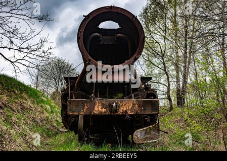 Locomotiva a steem arrugginita con carrozza a carbone abbandonata al cimitero dei treni sul vecchio binario ferroviario. Foto Stock