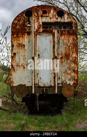 Vecchio carro merci arrugginito abbandonato sul fianco ferroviario con erba verde Foto Stock