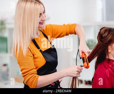 Il parrucchiere con vista ravvicinata avvolge i ricci con un ferro da stiro nel salone. Acconciatura professionale Foto Stock