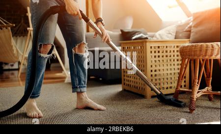 Ragazza che pulisce la moquette con l'aspirapolvere dalla polvere a casa. Donna domestica con hoover che fa ordine nell'appartamento Foto Stock