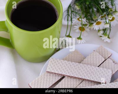 Un tovagliolo bianco con una tazza verde con caffè, un piatto di waffle e fiori Foto Stock