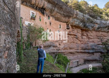 Uomo maturo in piedi e ammirando a El Puig de la Balma, a Mura (Spagna), un'antica casa colonica del XII secolo scavata nella roccia locale. Foto Stock