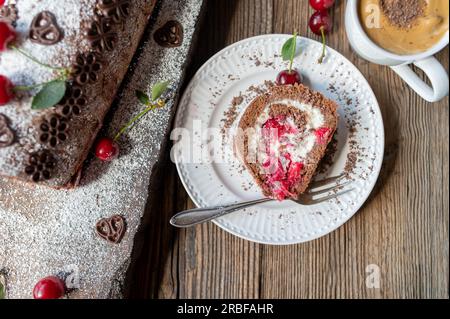 Rotolo svizzero con crema e ciliegie su fondo di legno. Deliziosa torta di ciliegie al cioccolato Foto Stock