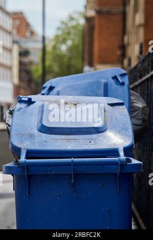 9 luglio 2023 - LondonUK : bidoni blu traboccanti con coperchio incollato e fodere nere dei bidoni Foto Stock