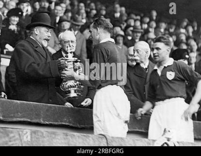 Londra, Inghilterra: 1930 King George of England presenta il trofeo della Football Association a Mr. Parker, il capitano degli Arsenals che ha vinto la finale di Coppa allo stadio di Wembley. Foto Stock