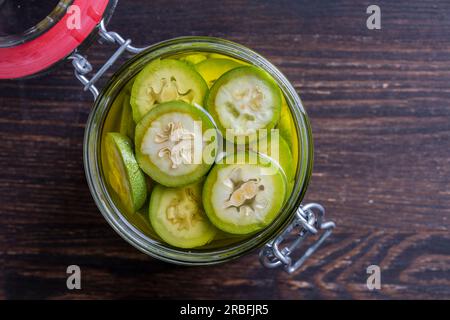 Noci non mature a fette in alcool in un vaso, per preparare la tintura fatta in casa, primo piano. Tintura di noci verdi in un vaso di vetro su un tavolo di legno, vie superiori Foto Stock