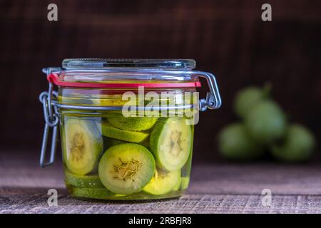 Noci non mature a fette in alcool in un vaso, per preparare la tintura fatta in casa, primo piano. Tintura di noci verdi in un vaso di vetro su un tavolo di legno Foto Stock