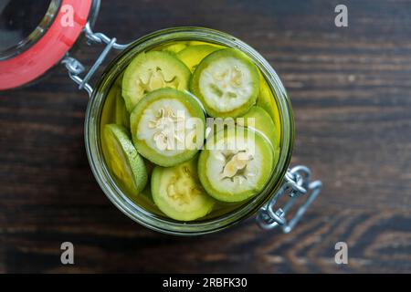 Noci non mature a fette in alcool in un vaso, per preparare la tintura fatta in casa, primo piano. Tintura di noci verdi in un vaso di vetro su un tavolo di legno, vie superiori Foto Stock