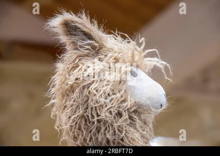 Simpatica testa di lama giocattolo sfocata su sfondo marrone chiaro - tagliata Foto Stock