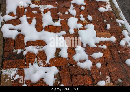 La neve si scioglie, ma è ancora visibile nei blobi sul marciapiede di mattoni in mattoni parzialmente rotti Foto Stock