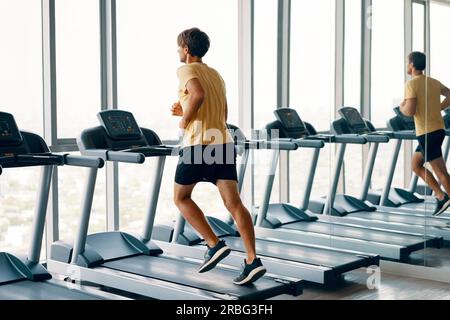 A piena lunghezza Ritratto di giovane uomo di sport in esecuzione su un tapis roulant in palestra. Fitness e di allenamento e di uno stile di vita sano concetto. A piena lunghezza Foto Stock