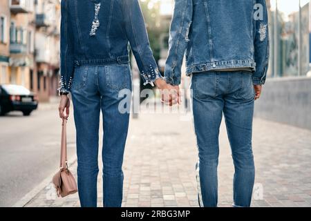 Giovane tenendo le mani nella strada della citta'. Vista posteriore di un uomo e di una donna che indossa jeans denim tenere mani e a piedi Foto Stock