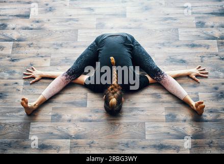 Vista superiore della giovane donna a praticare yoga facendo la tartaruga pongono. Kurmasana asana. Benessere e uno stile di vita sano Foto Stock