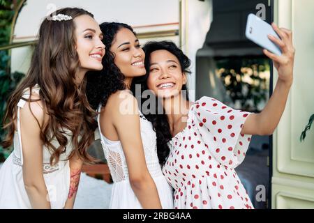 Bella donna sorridente tenendo selfie con il telefono cellulare. Multi etnico caucasico ragazze, africane americane ed asiatiche femmine rendendo self portrait durante Foto Stock