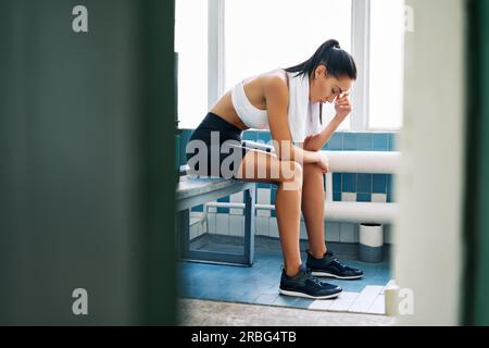 Donna stanca con un asciugamano nella stanza dell'armadietto dopo l'allenamento duro. Stress, sport, concetto di fallimento Foto Stock