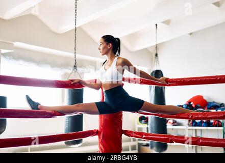 Giovane donna sportiva che fa le spaccature sulla cima della corda dell'anello di boxe. Esercizi di stretch Foto Stock