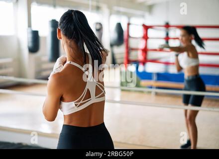 Vista posteriore della pugile femminile che fa la boxe ombra in palestra. Donna che fa pratica con i pugni e colpisce direttamente. Concetto sportivo Foto Stock