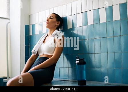 Donna stanca con un asciugamano nella stanza dell'armadietto dopo l'allenamento duro. Stress, sport, concetto di fallimento Foto Stock