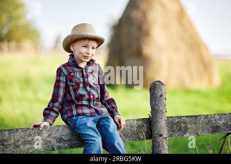 Primo piano ritratto di ragazzino in cappello sittingon recinzione in legno Foto Stock