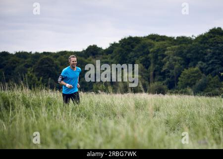 Montare l'uomo muscolare jogging su un sentiero rurale attraverso prati di indossare abbigliamento sportivo in uno stile di vita attivo concept Foto Stock