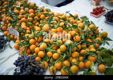 Clementine fresche con foglie verdi in vendita su un mercato degli agricoltori o store impilati su un tavolo Foto Stock