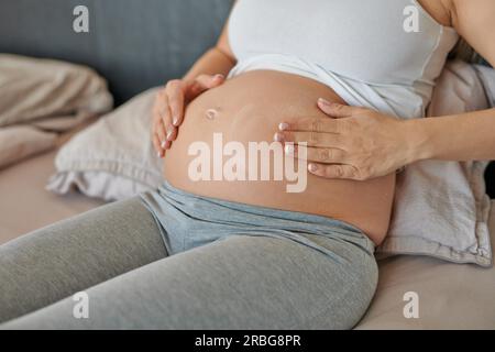 Giovane donna incinta sfregamento crema idratante sul suo ventre per idratare la sua pelle e ridurre la possibilità di smagliature dopo il parto Foto Stock