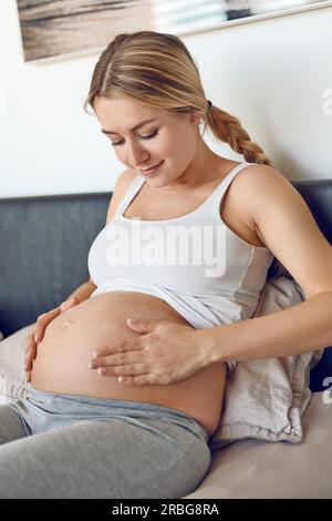 Giovane donna incinta sfregamento crema idratante sul suo ventre per idratare la sua pelle e ridurre la possibilità di smagliature dopo il parto Foto Stock