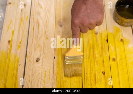 applicare la composizione protettiva sul tabellone con una spazzola. trattamento del legno da marciume. il maestro dipinge tavole di legno. Foto Stock