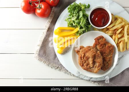 Gustosi schnitzels serviti con patatine fritte, ketchup e verdure su un tavolo di legno bianco, piatti. Spazio per il testo Foto Stock