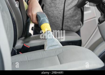 Sedile anteriore in tessuto per auto con aspirapolvere per uomo. uomo che pulisce la macchina da lavoro Foto Stock