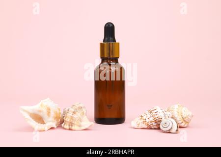 Siero in flacone di vetro marrone senza marchio con pipetta e molte conchiglie su sfondo rosa. Flacone cosmetico per la marcatura di farmaci o co Foto Stock