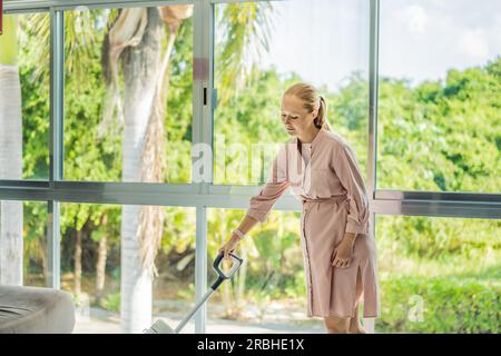 La giovane donna incinta ama pulire la sua casa. Facile pulizia con un aspirapolvere wireless. Donna incinta che pulisce il pavimento con l'aspirapolvere portatile Foto Stock