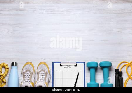 Formazione personale. Clipboard con piano di allenamento, scarpe da ginnastica e attrezzature sportive su un tavolo in legno bianco, piatto. Spazio per il testo Foto Stock