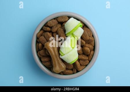 Cibo secco per cani e dolcetti (masticare le ossa) su sfondo azzurro, vista dall'alto Foto Stock