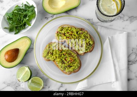 Deliziosi panini con guacamole e ingredienti su un tavolo in marmo bianco, piatti Foto Stock