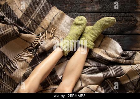 piedi da donna in calze calde su un motivo a quadri di lana sul pavimento, piedi sul pavimento a casa, comfort a casa Foto Stock