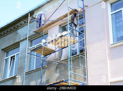 Appaltatori edili che dipingono muri all'esterno della facciata della casa. Primo piano sul muro esterno della casa di verniciatura durante la ristrutturazione della casa. Foto Stock