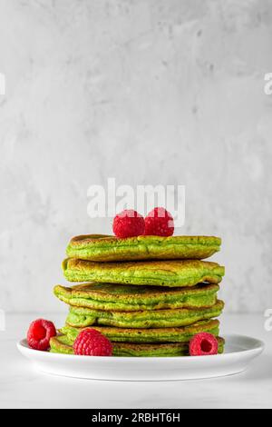 Pila di pancake fatti in casa con tè matcha, lamponi freschi, pistacchi su sfondo bianco Foto Stock